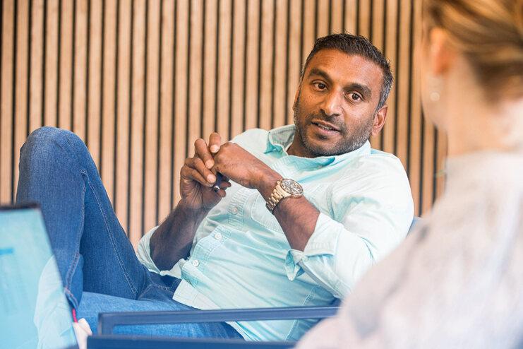 Mann im hellblauen Hemd sitzt entspannt mit gefalteten Händen während eines Gesprächs in einem modernen Raum.