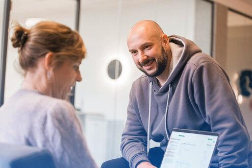 Zwei Personen führen ein Gespräch, während ein Laptop mit geöffnetem Dokument zwischen ihnen steht.